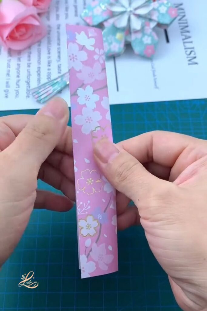 Both hands holding the folded white paper strip upright