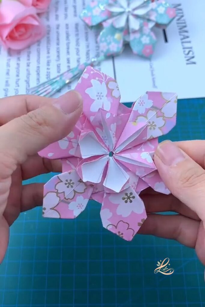 Both hands pressing the white inner flower layer into the centre of the completed pink outer flower, the two-layer composition visible with the white petals nestled inside the larger pink ones