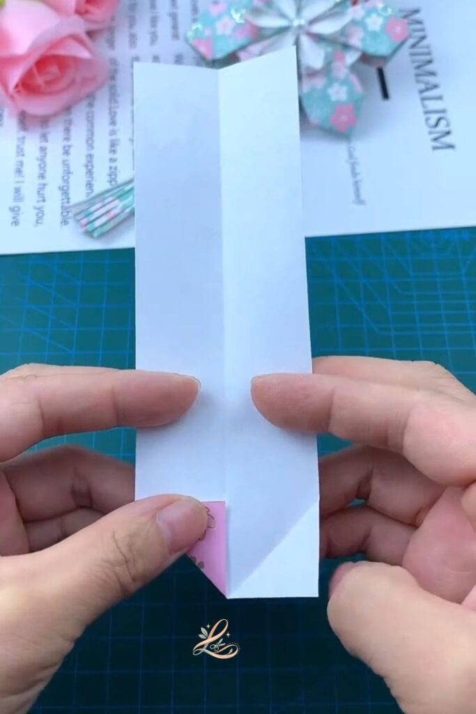 The paper held front-facing, the two bottom corners folded inward to a clear downward diamond point, both crease lines crisp and visible