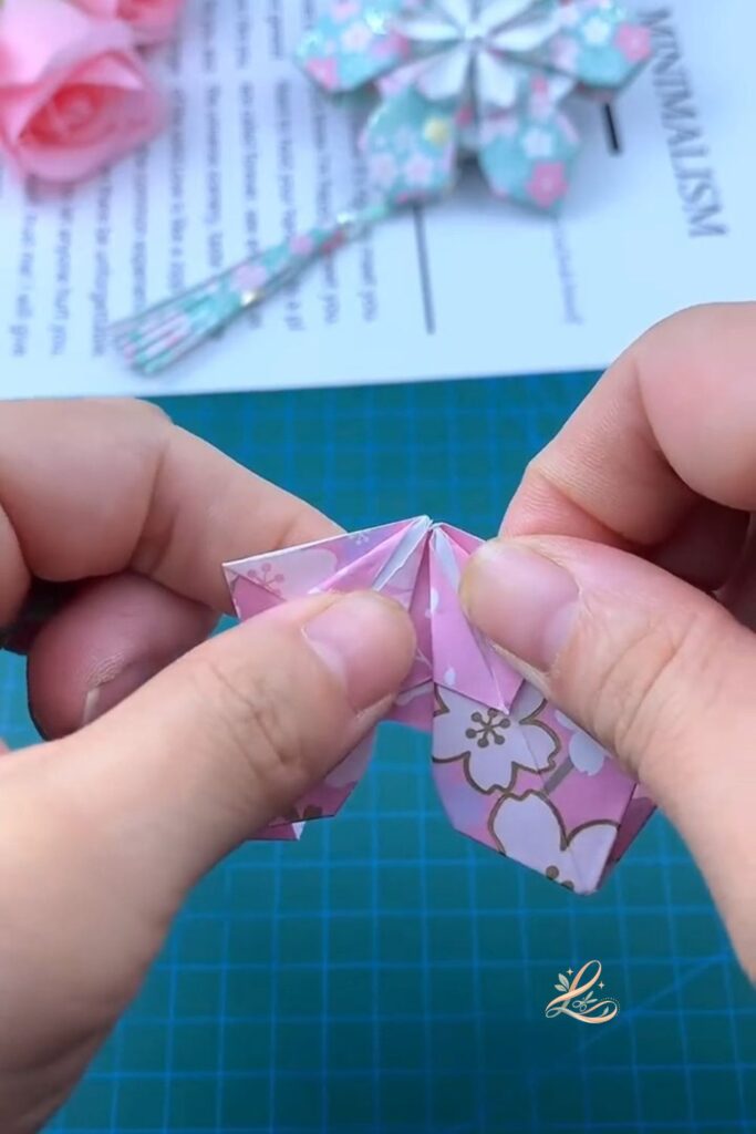 Two modules pressed together in both hands, the glue stick visible to one side, the two-petal fan shape clearly showing with the petals angled outward from the joined centre