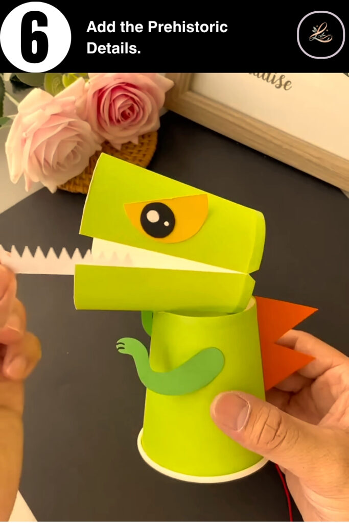 Completed paper cup dinosaur puppet with teeth and spikes.