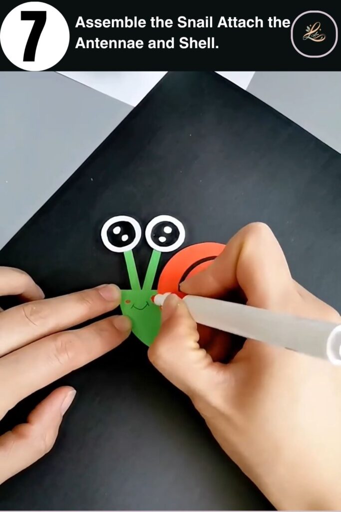 Assembling a DIY paper snail by attaching antennae and shell to the green cardstock body