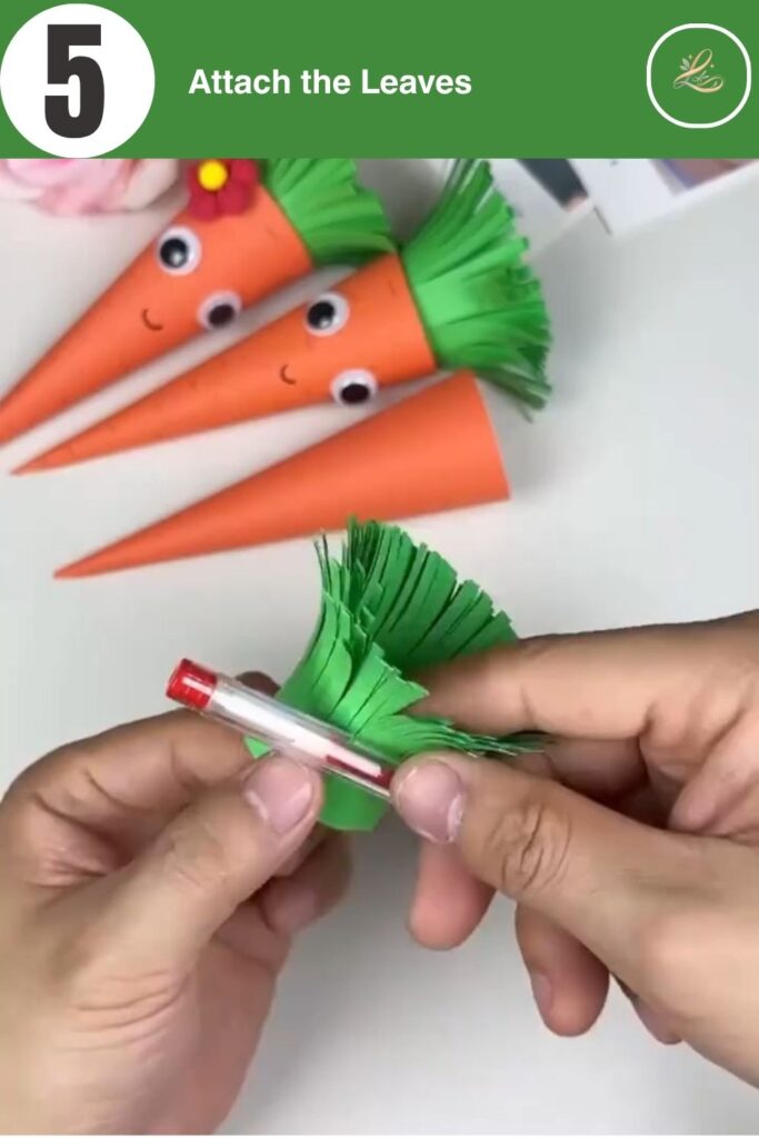 Attaching green paper leaves to the top of an orange paper cone.