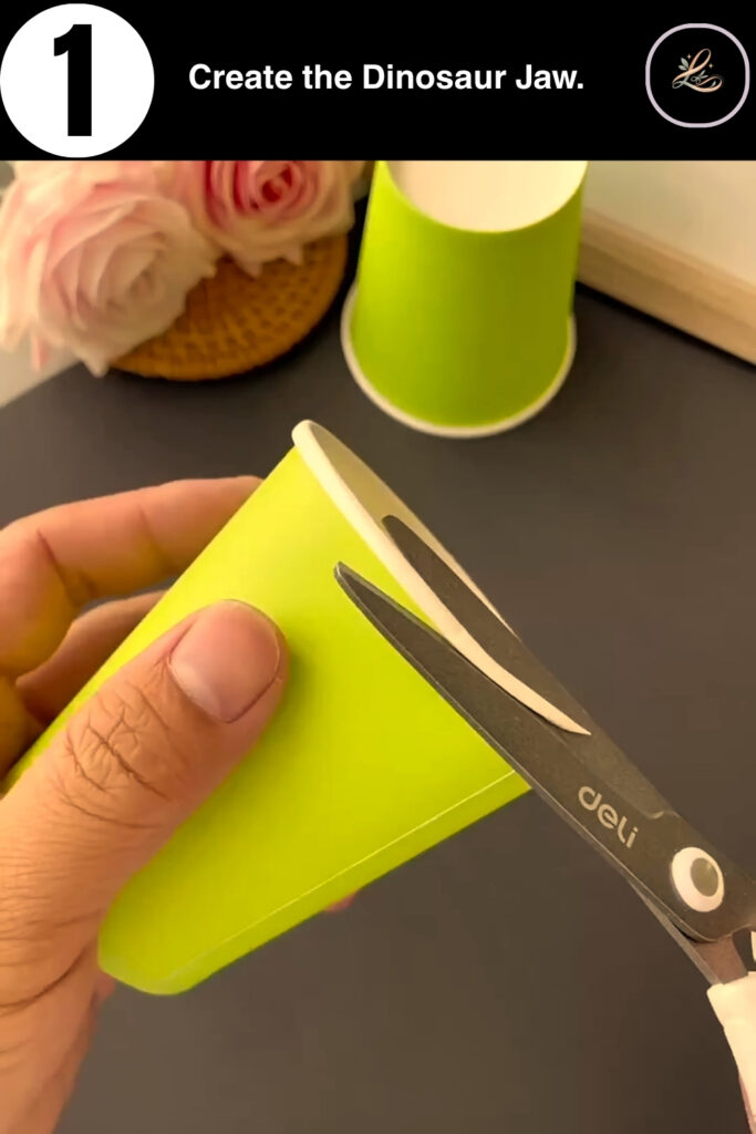 Cutting a V-shape into a green paper cup for a dinosaur mouth.