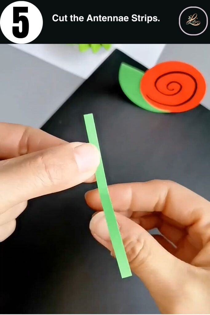 Two thin green paper strips held in a V-shape to form snail antennae for a DIY paper craft