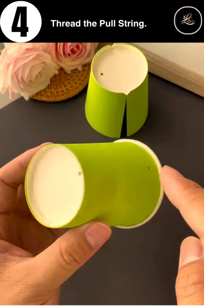 Threading red string through a hole in a green paper cup.