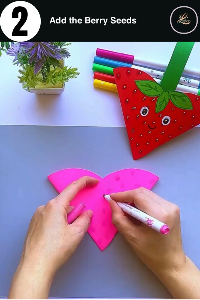 Drawing seed patterns on a pink paper strawberry using a marker.