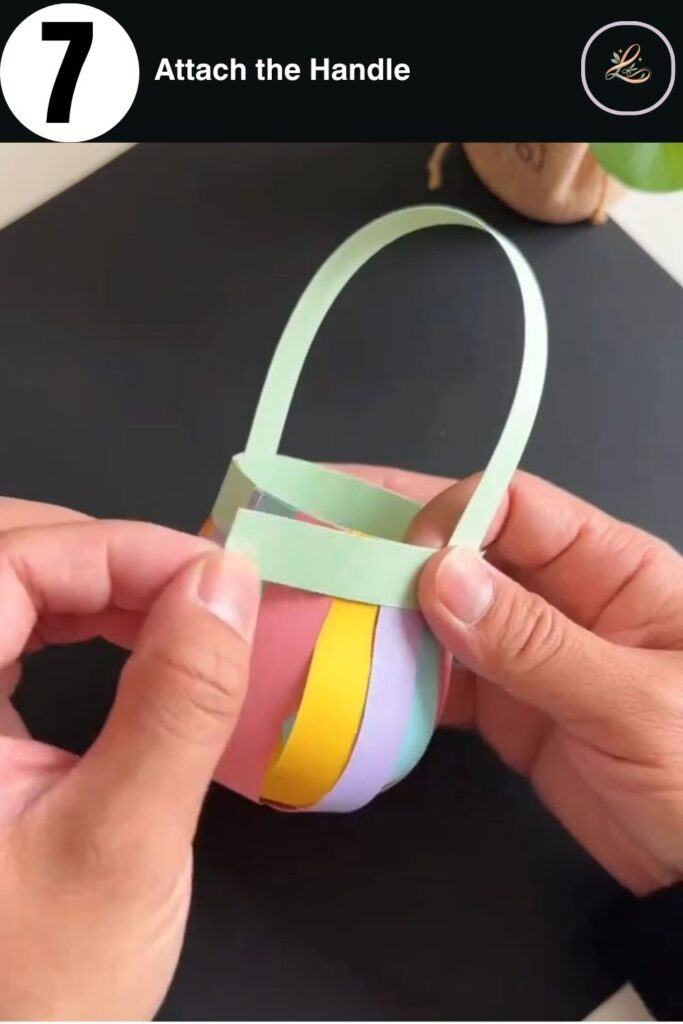 Mint green paper handle attached to a colorful paper strip basket, showing the completed handle arch in a kids paper craft tutorial