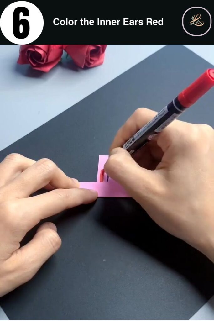 Red marker coloring the inner ears of a pink paper bunny ring craft project
