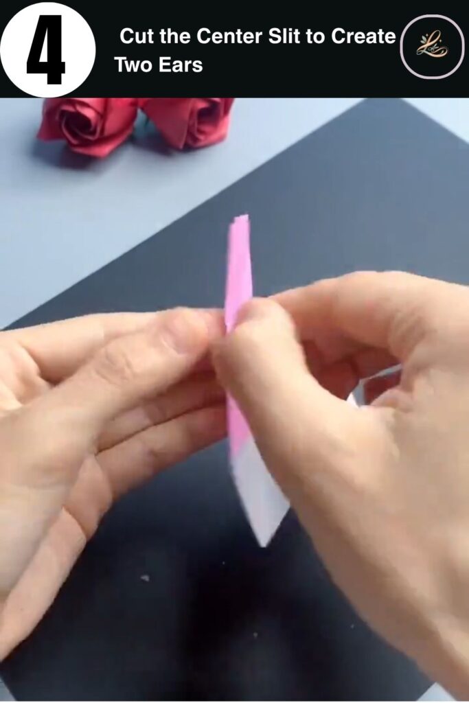 Scissors cutting a center slit in folded pink paper to create two bunny ears for a paper finger ring