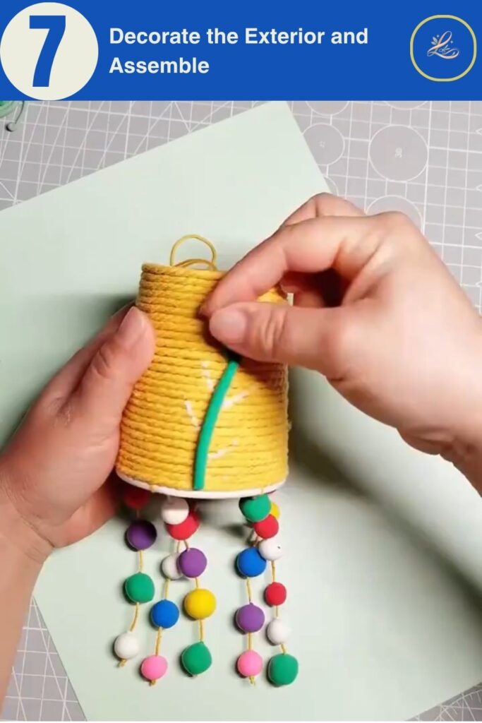 Colorful Cup Wind Chime Mobile for Beginners (DIY Decor) Attaching a small clay vine detail onto a yellow yarn-wrapped chime cup.