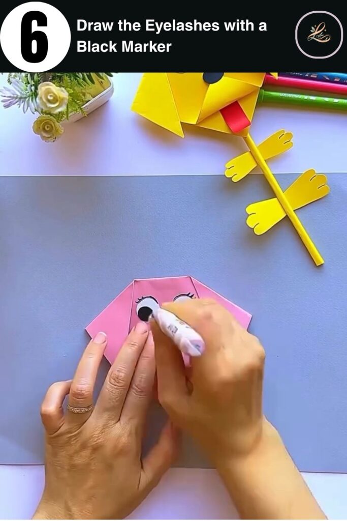 Drawing eyelashes on a paper dog craft with a black marker, adding detail to a DIY pencil topper
