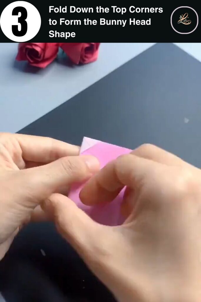 Pink paper folded into a peaked triangle shape showing the bunny head form for a paper ring craft