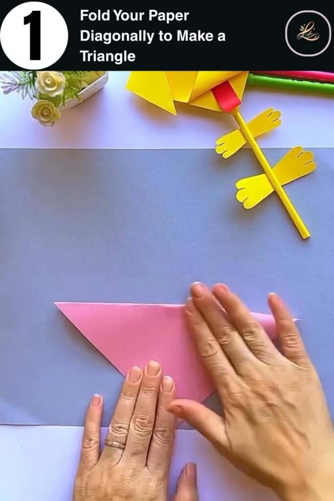 Hands folding pink cardstock diagonally into a triangle to start making a paper dog pencil topper