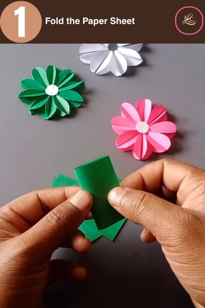 Pretty Paper Daisy Flower Craft for Kids A hand folding a small green rectangular piece of paper in half lengthwise to create a clean crease.