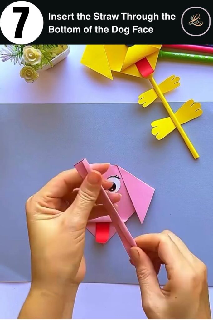 Inserting a pink straw into the bottom of a paper dog face to create a DIY paper dog pencil topper