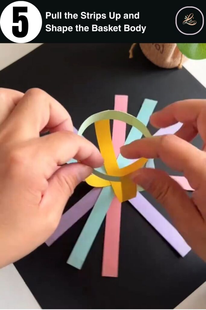 Colorful paper strips being pulled upward to form the round body of a paper basket in a kids craft tutorial