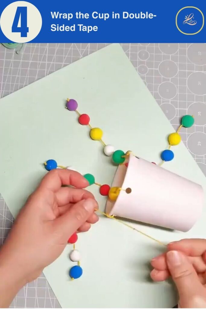 Colorful Cup Wind Chime Mobile for Beginners (DIY Decor) Applying double-sided tape to the outside of a paper cup.