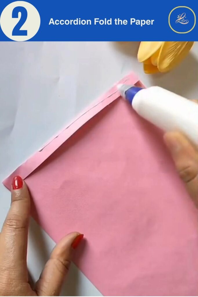 Hands holding accordion-folded pink cardstock showing even pleats for DIY paper gift bag