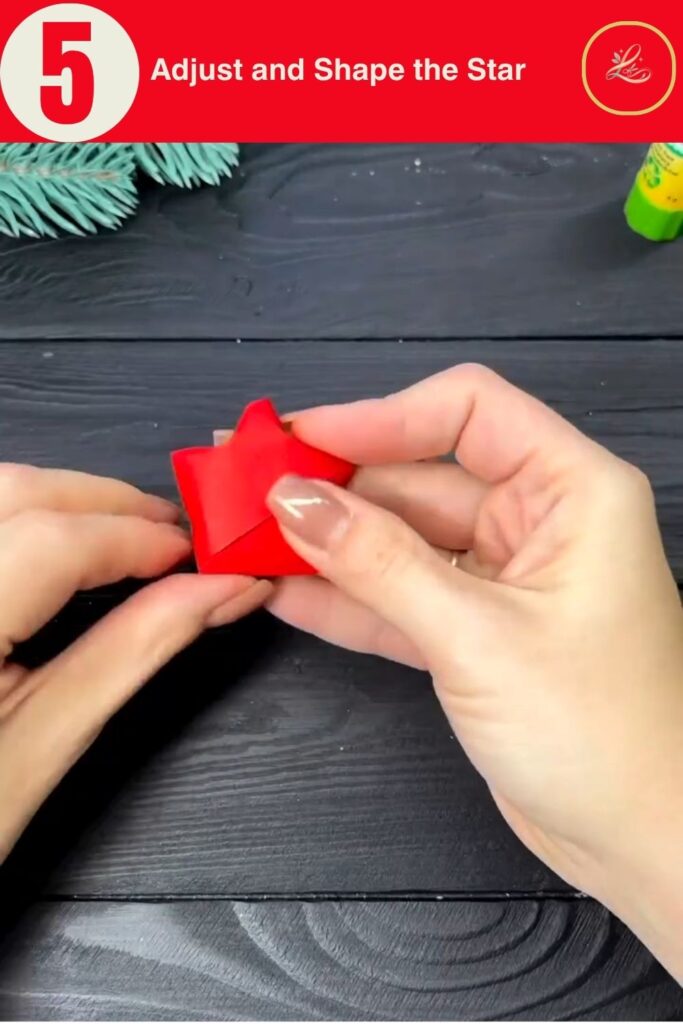 Hand holding a puffed red paper star showing its five points, shaping step in a DIY Christmas ornament tutorial