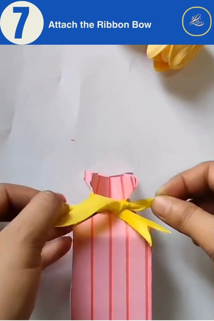 Hands tying a yellow ribbon bow around a handmade pink birthday paper gift bag