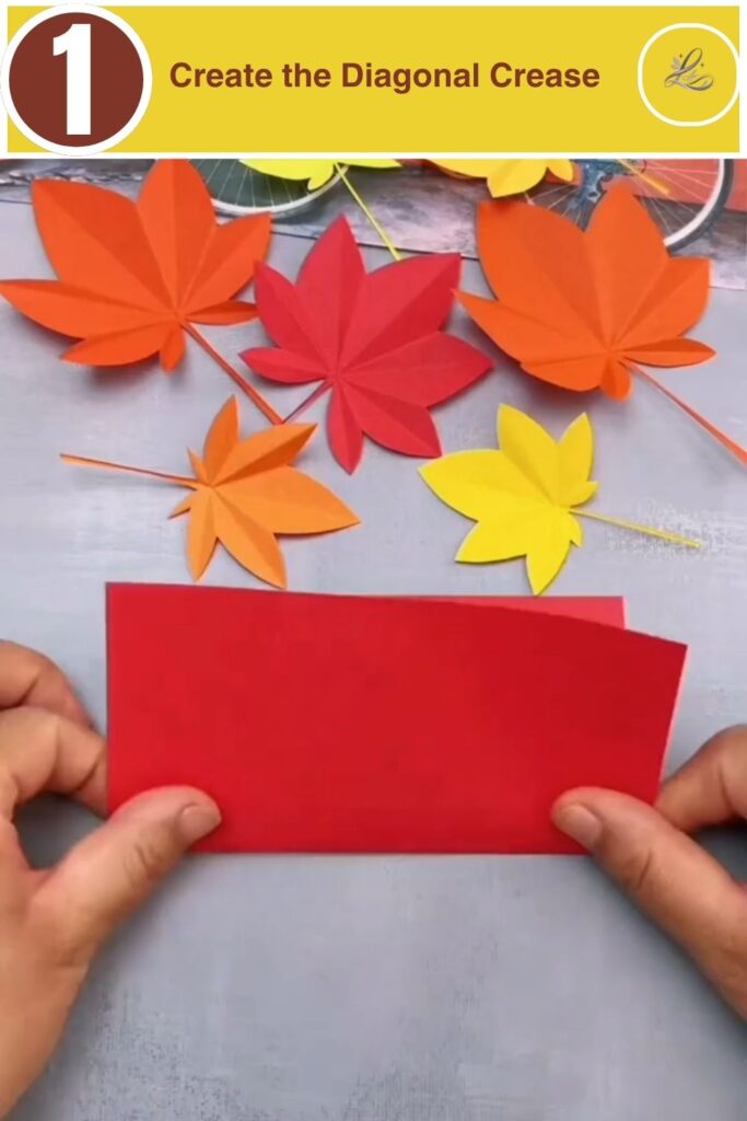 A square piece of red craft paper being folded diagonally to create a central crease.