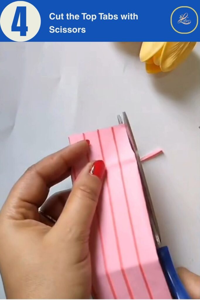 Scissors cutting angled tabs into the top of folded pink paper to make a DIY gift bag closure