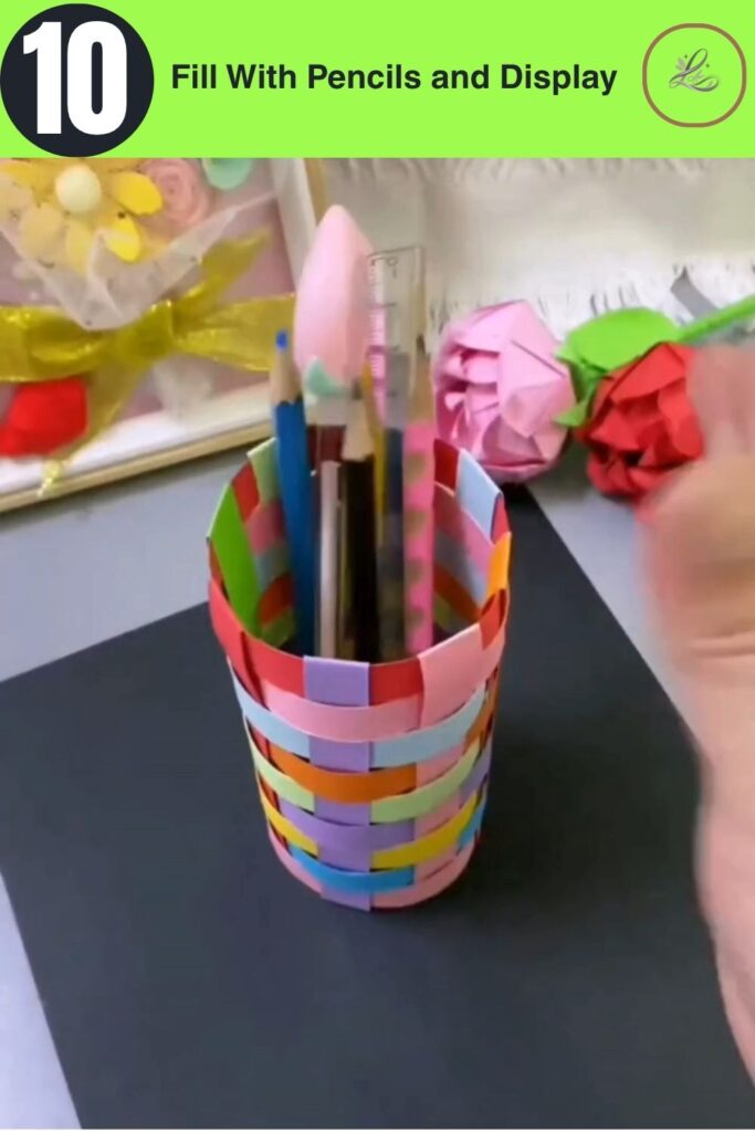 Fun Rainbow Woven Paper Pencil Holder DIY (#1) Finished DIY rainbow woven paper pencil holder standing on a craft desk filled with colored pencils, a ruler, and a paintbrush