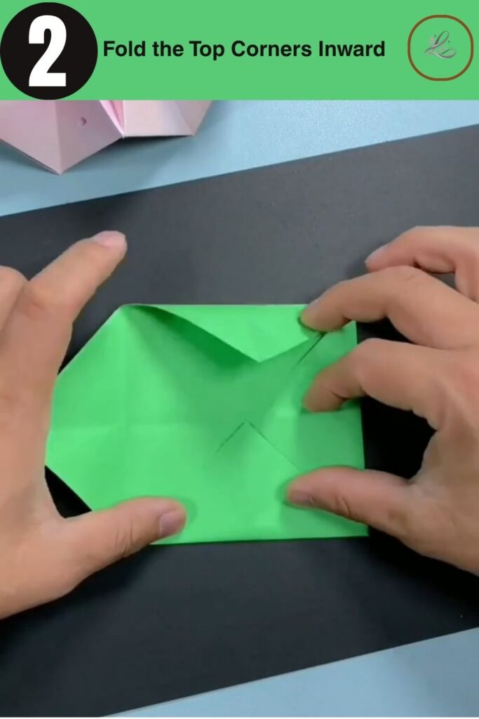 Folding top corners of origami paper inward to meet the center line.