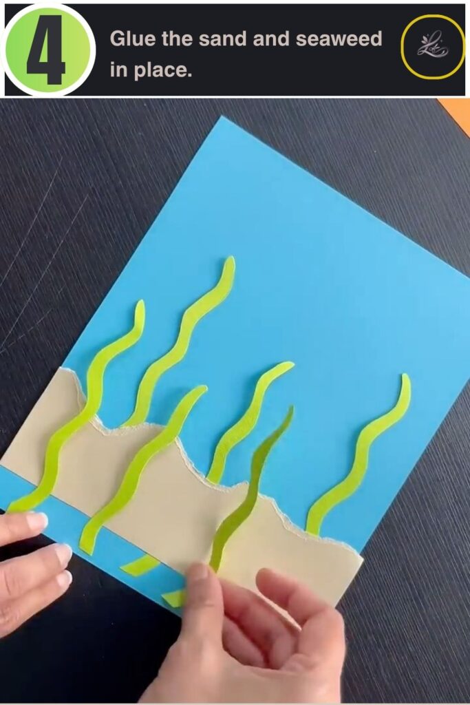 Sand and seaweed glued onto a paper ocean background for a kids craft
