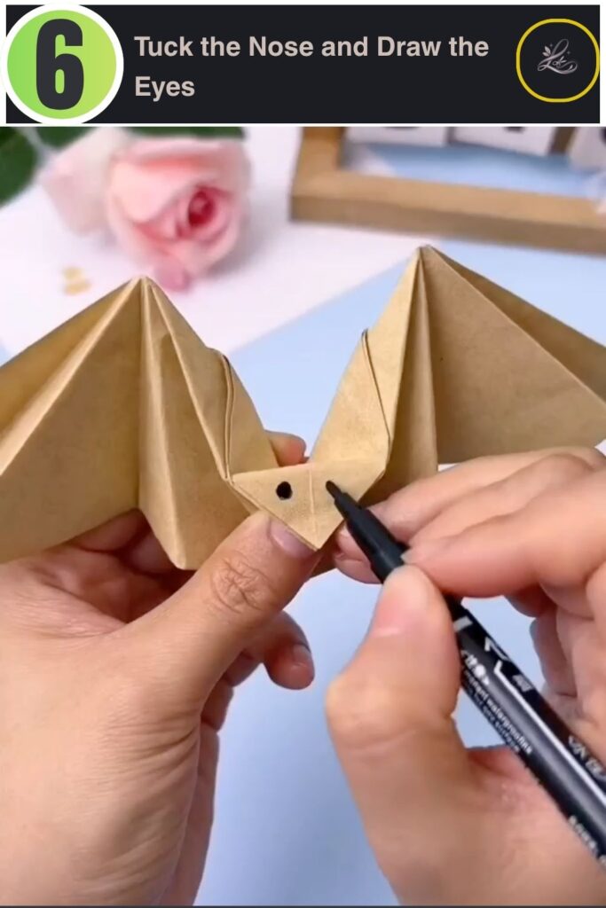 Drawing eyes onto the finished origami bat craft to complete the face.