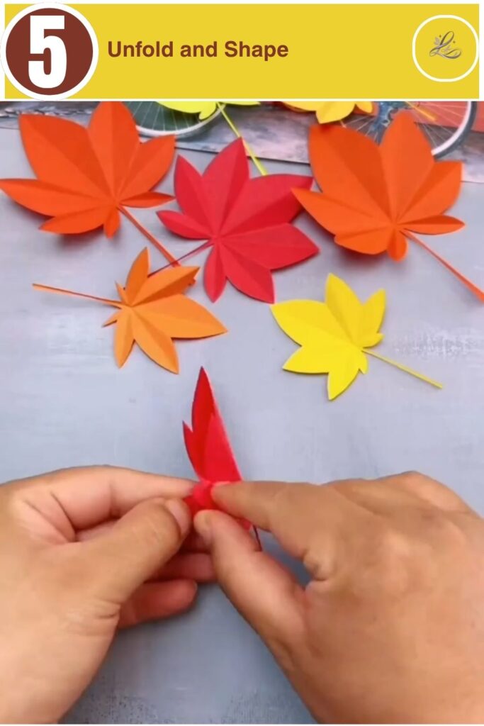 Finished red paper maple leaf being displayed open on a gray background.
