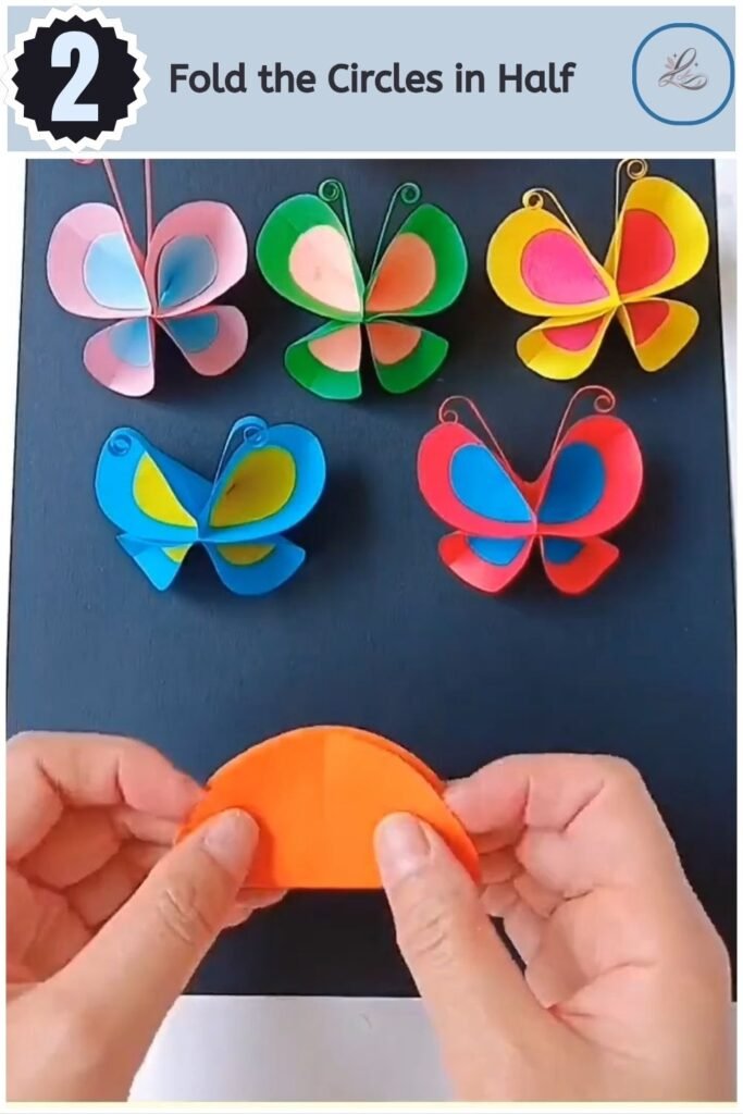 A hand folding stacked orange and blue paper circles in half.