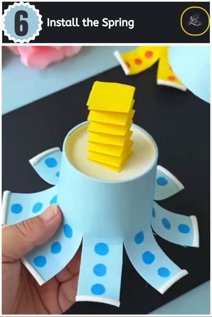 Playful Paper Cup Octopus Craft for Beginners Securing a yellow paper spring inside a blue paper cup octopus craft.