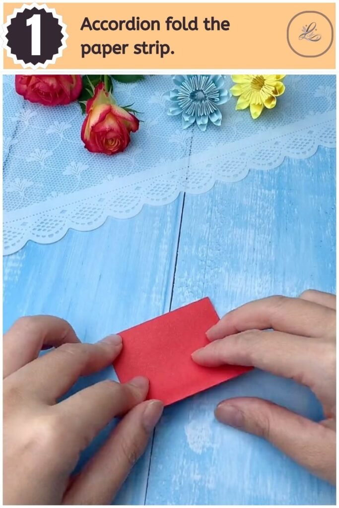 Hands accordion folding a rectangular strip of red craft paper on a blue background.
