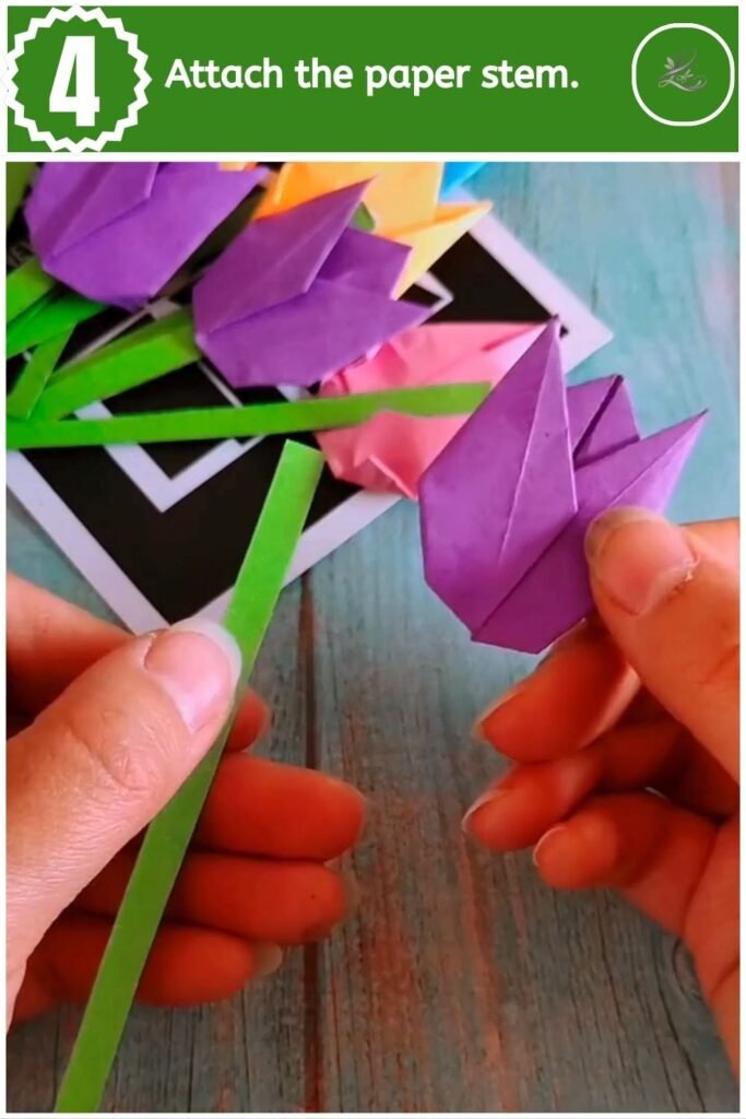 Attaching a thin green paper stem to the base of a folded purple paper tulip.