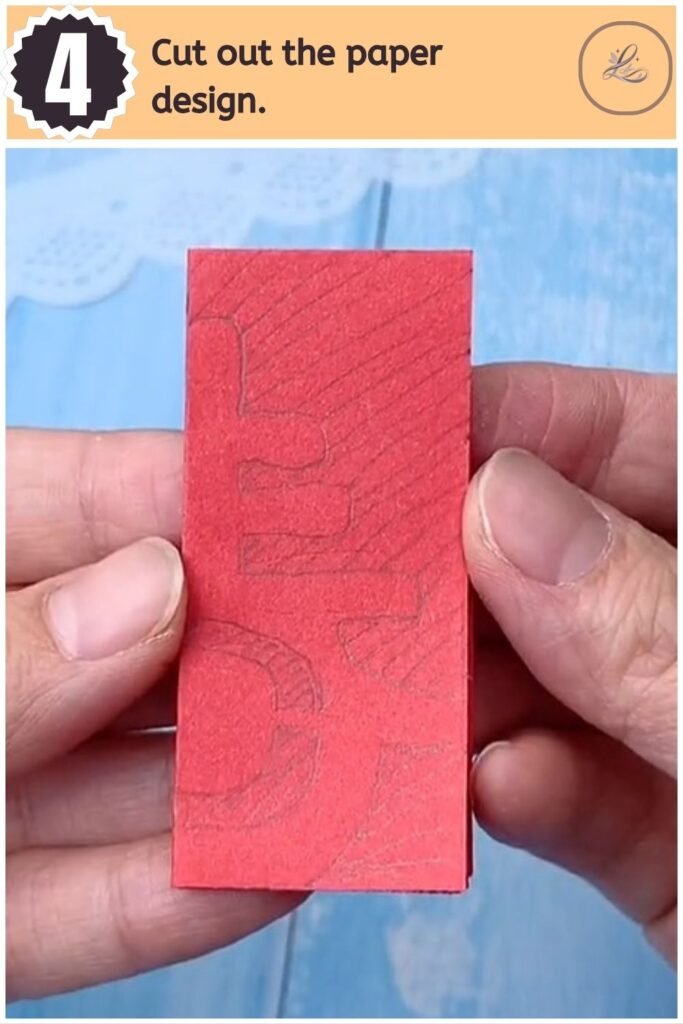 Scissors cutting out the pencil design along the edges of folded red paper.