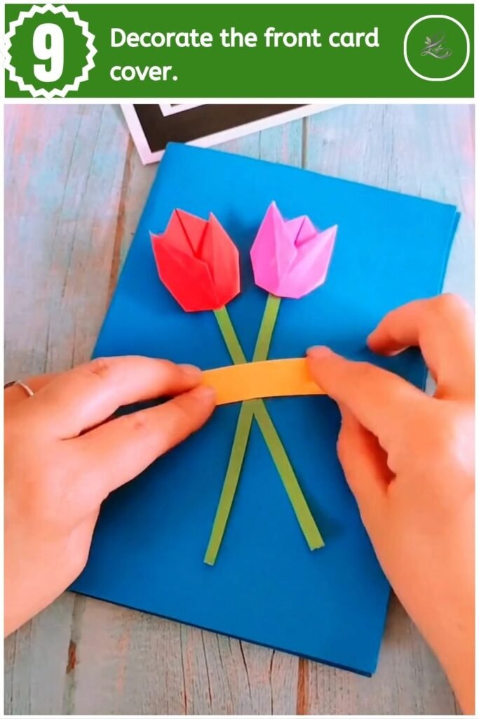 Glueing two paper tulips and a yellow banner onto the front cover of the blue greeting card.