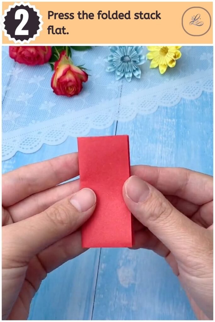 Stacked rectangle of folded red paper held flat between fingers.