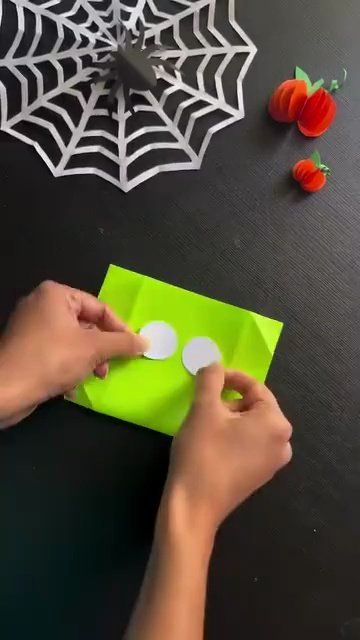 Gluing white paper eyes and black eyebrows onto green craft paper